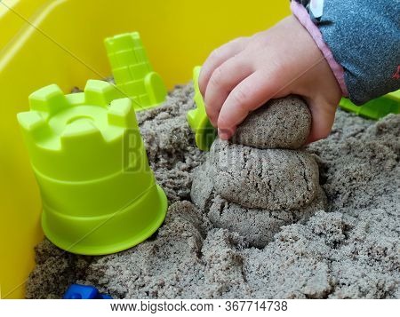 The Child Makes Of A Sandyman From Kinetic Sand. Pictured Is A Child's Hand Holding Sand And Plastic