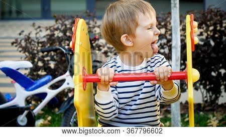 Funny Portrait Of Little Boy Riding On Chidlren Playground And Showing Tongue