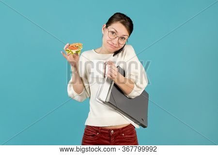 Smiling Office Employee Holds The Phone With Her Shoulder, Drinks Coffee, Eats A Sandwich. Overload 