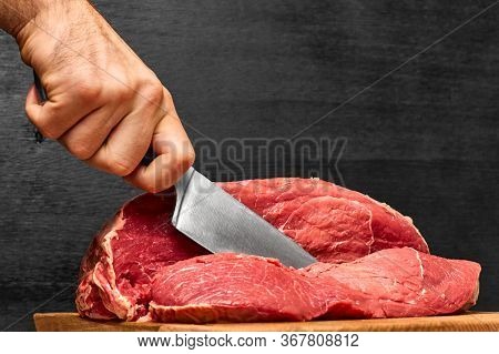 Closeup Man Hand Cutting A Beef Meat With A Knife On A Black Background. Concept Of Healthy Protein 