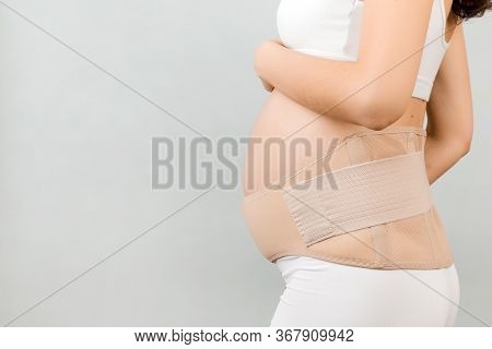 Side View Of Pregnant Woman In Underwear Wearing Pregnancy Bandage At Gray Background With Copy Spac