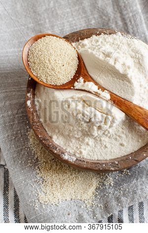 Raw Fonio Flour In A Bowl And Seeds In A Spoon On Grey Napkin Top View. Alternative Flour