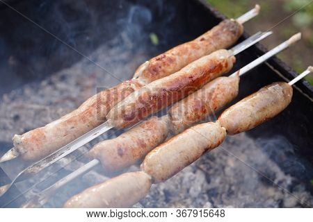 Close Up Of Toasted Sausages On Skewers. Succulent Kupaty Roasting On Chargrill. Concept Of Picnic O