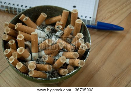 Špinavý popelník plný nedopalky cigaret na dřevěný stůl