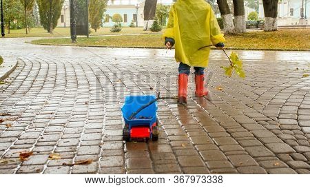Closeup Photo Of Little Boy Pulling Hif Toy Truck In Park On Rainy Autumn Day