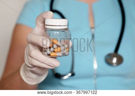 Doctor With Pills, Woman In Medical Mask And Latex Gloves Giving Bottle Of Capsules. Concept Of Dose