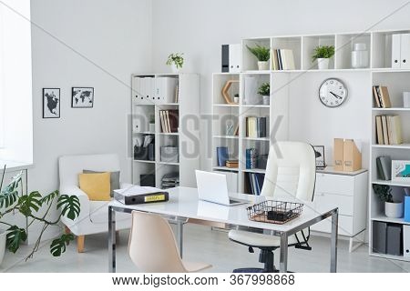 Office of business person with desk, armchair of professional, chair for clients, shelves, clock, green plant and two pictures on wall