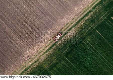 Aerial Shot Of Agricultural Tractor With Crop Seeder Attached Driving Along Dirt Road Through Plowed