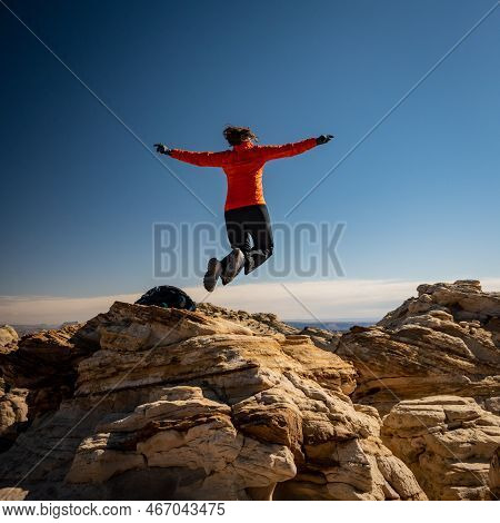 Woman In Orange Jacket Jumps On Top Of High Rocks In Capitol Reef National Park