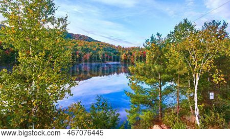 Looking Through Trees Elevated View Of Blue Foggy Morning Lake Surrounded By Fall Mountains