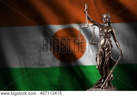 Niger Flag With Statue Of Lady Justice And Judicial Scales In Dark Room. Concept Of Judgement And Pu