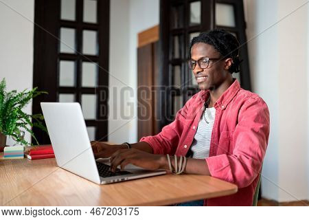 Happy Satisfied Young African Guy Freelancer Sitting At Home Office Using Laptop, Looking At Compute