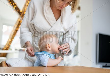Casual Domestic Lifestyle Moments Concept. Infant Baby Boy Drinking Water From Small Glass With A He