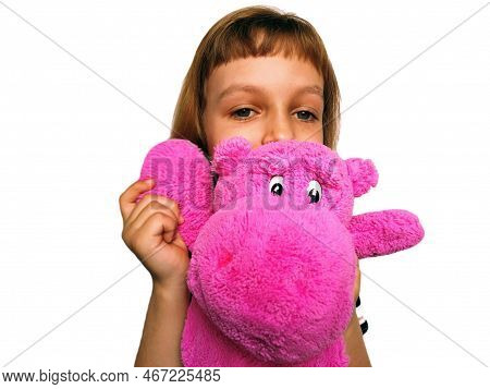 A Cute Caucasian Girl Of 7 Years Old With Blond Hair Cuddles And Hugs A Pink Hippopotamus. Hippo Plu