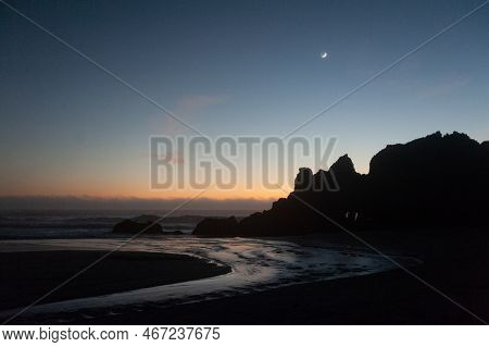 A Cresent Moon Accentuates The Beach During The Golden Hour After Sunset.