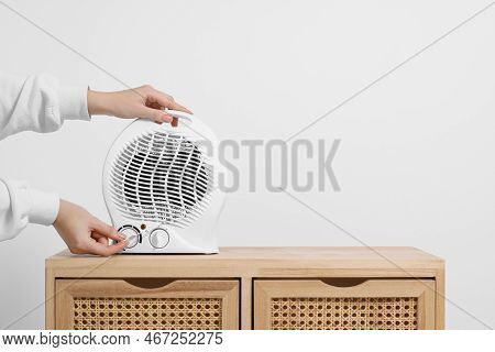 Woman Turning On Electric Fan Heater Indoors, Closeup. Space For Text