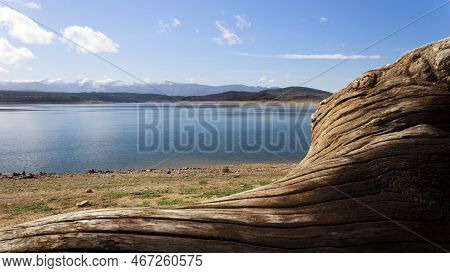 View Of The Barcena Reservoir With The Montes Aquilanos Mountain Range At Background And A Driftwood