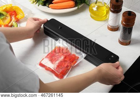 Woman Using Sealer For Vacuum Packing With Plastic Bag Of Red Pepper At White Table, Closeup