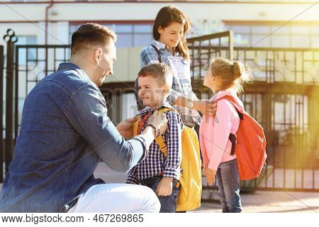 Young Parents Saying Goodbye To Their Little Children Near School