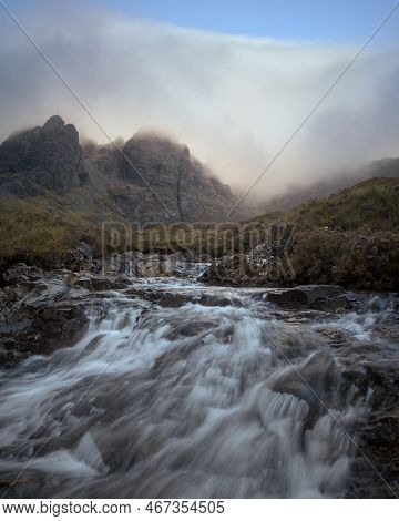Morning View Of River In The Foreground And Cloud Covered Mountain Range. Scenic Summer Landscape Wi