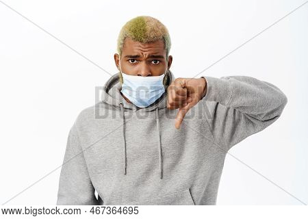 Covid 19, Coronavirus Concept. Black Man Shows Wrong Way Of Wearing Medical Face Mask, Makes Thumbs 