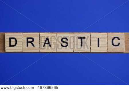Word Drastic Made From Wooden Gray Letters Lies On A Blue Background