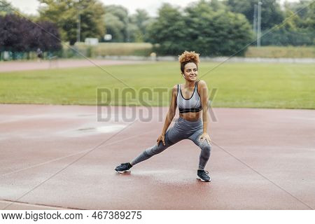 A Happy, Slim Runner Stretching Her Legs And Warming Up While Standing In The Stadium On A Rainy Day