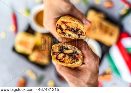 Hands Holding Mexican Burritos With Chicken, Rice, Beans,cheese Served With Sauce Borracha