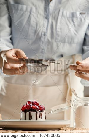 A Girl In An Apron In The Kitchen Sprinkles Sugar On A Cupcake. The Housewife Is Preparing A Cupcake