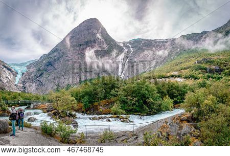 Briksdalen, Norway - August 22 2022: The Briksdalselva River With The Footbridge And The Briksdalsbr