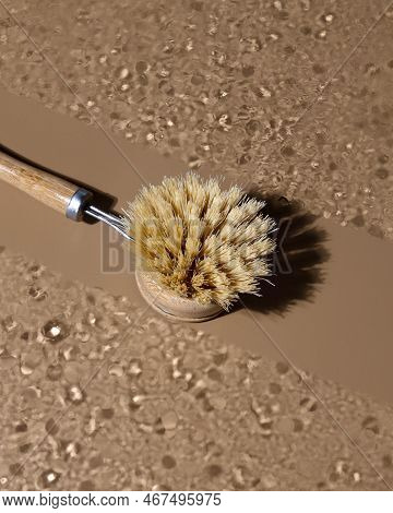 Eco-friendly Bamboo Dishwashing Brush With Long Wooden Handle Lying On Glass With Whater Drops.