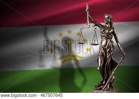 Tajikistan Flag With Statue Of Lady Justice And Judicial Scales In Dark Room. Concept Of Judgement A
