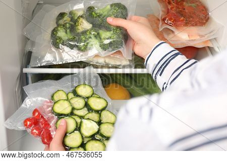 Woman Putting Vacuum Bags With Vegetables Into Fridge, Closeup. Food Storage