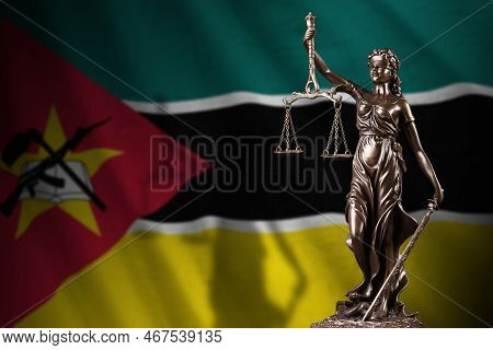 Mozambique Flag With Statue Of Lady Justice And Judicial Scales In Dark Room. Concept Of Judgement A