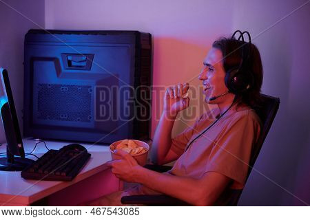 Joyful Young Man Eating Potato Chips When Watching Stream Or Letsplay Video On Computer At Home