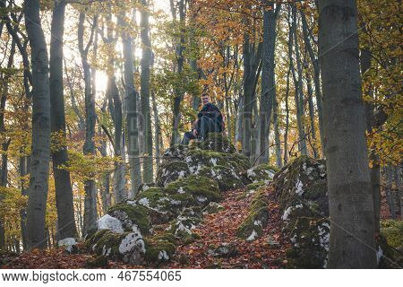 Adventurer Sitting On A Rock In Autumn Forest In Strazovske Mountains, Slovakia. A Man With A Smile 