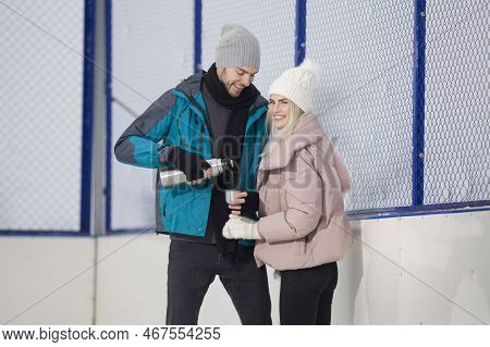 Young Caucasian Couple In Love In Winter With Ice Skates Posing Together With Vacuum Flask In Snowy
