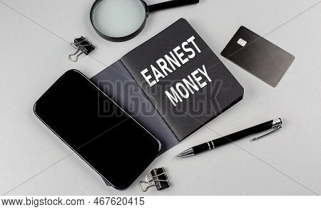 Earnest Money Text Written On A Black Notebook With Smartphone, Magnifier And Credit Card