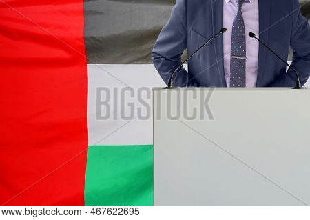 Tribune With Microphone And Man In Suit On Flag Of United Arab Emirates Background. Businessman And 