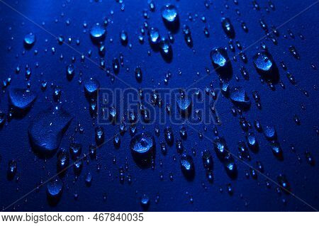 Round Drops Of Water On Dark Blue Background. Through Transparent Drops Of Water Pass Rays Of Light.