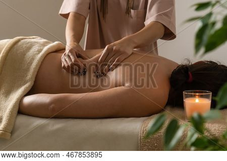 Masseur Does A Back Massage In The Cozy Atmosphere Of The Spa Salon With Green Plants, A Burning Can