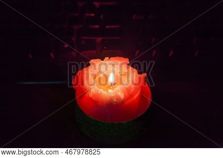 Burning Thick Short Red Candle On The Table Against The Keyboard During A Blackout