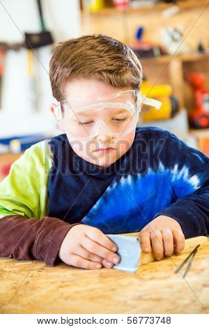 Boy Sanding Wooden Block In Workshop As He Builds Car For Pinewood Derby