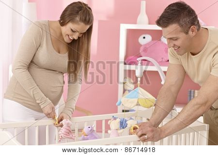 Pregnant mother and husband preparing baby's cot, smiling.