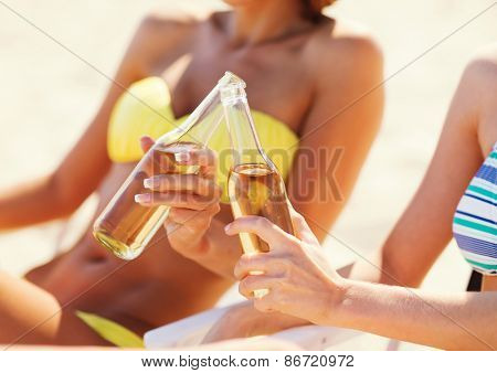 summer holidays and vacation - two girls in bikinis with drinks on the beach chairs