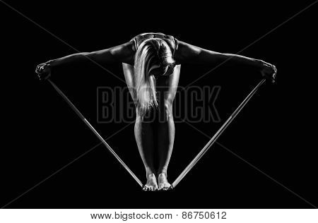 Sportswoman exercising with a resistance band on black background.