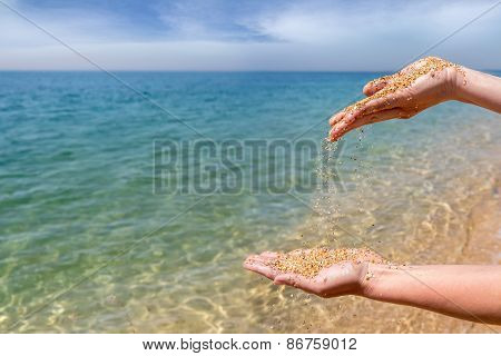 Female Hands Pouring Coral Sand On The Sea Background