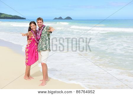 Portrait of couple of tourists happy standing on Hawaiian beach at their Hawaii vacation. Asian woman and Caucasian man wearing flower lei garland and Aloha clothing showing Shaka hand sign on travel.