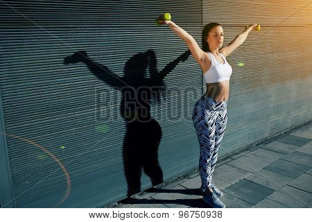 Sporty young woman lifting weights standing with arms outstretched against black wall background