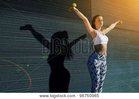 Athletic female with perfect figure getting her arms in great shape while lifting weights at outdoor